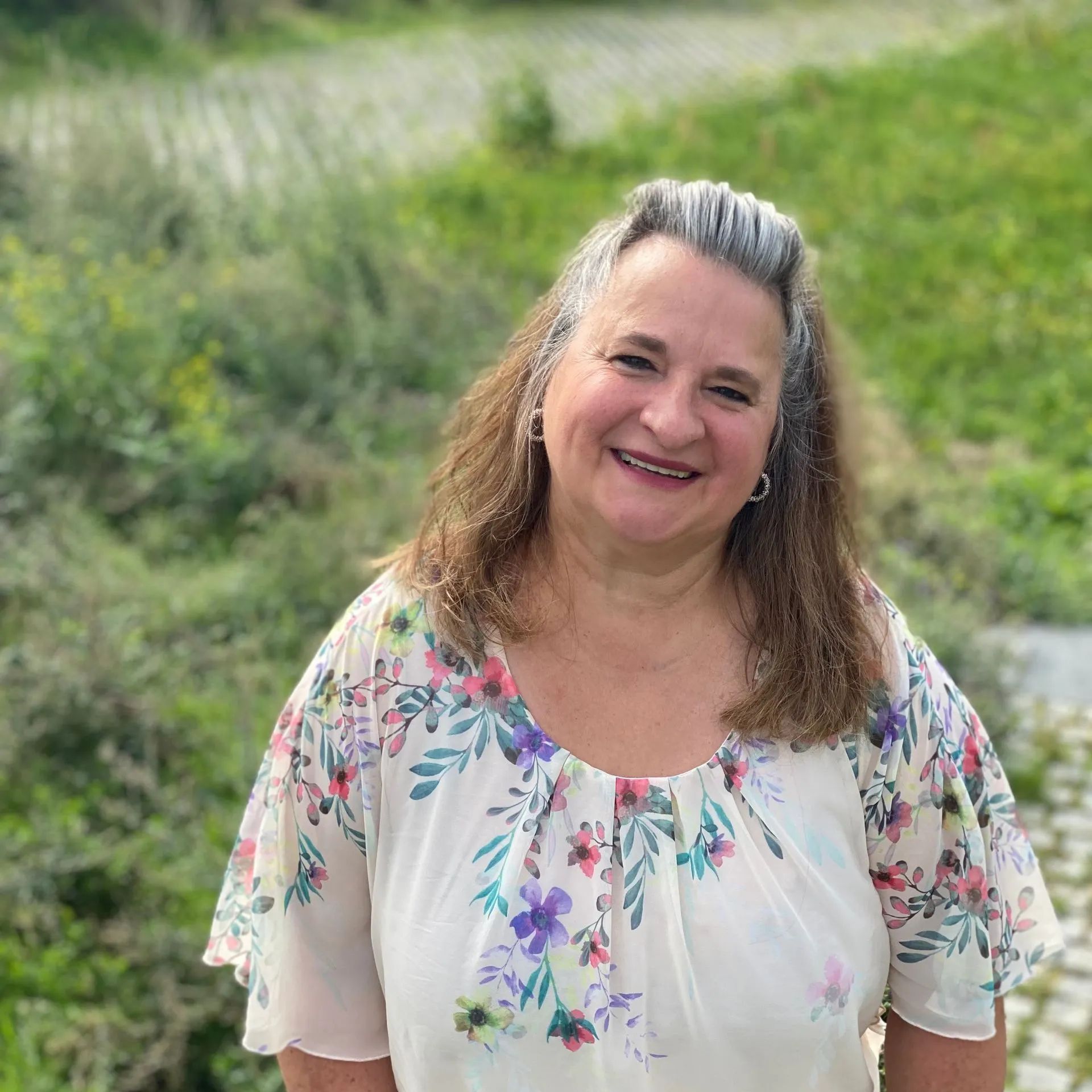 Eine Frau in einer geblümten Bluse lächelt in die Kamera.
