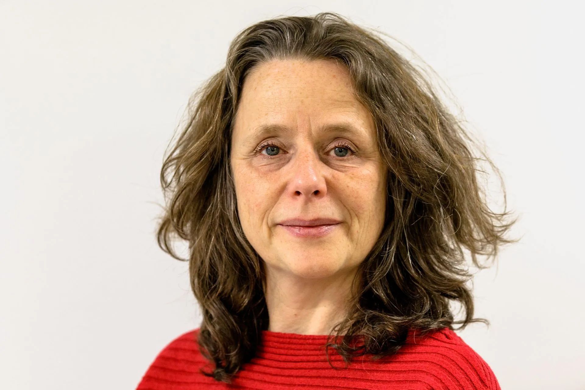 Eine Frau mit langen braunen Haaren trägt einen roten Pullover und lächelt.