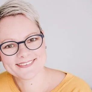 Eine Frau mit Brille und gelbem Hemd lächelt in die Kamera.