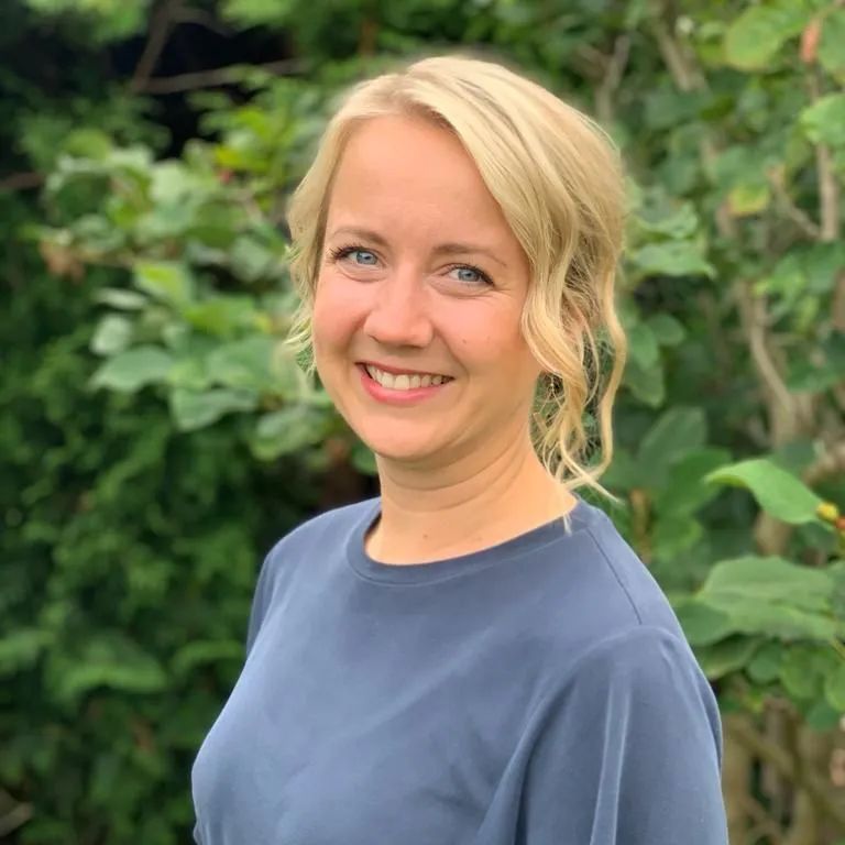 Eine Frau in einem blauen Hemd lächelt vor einem Baum.