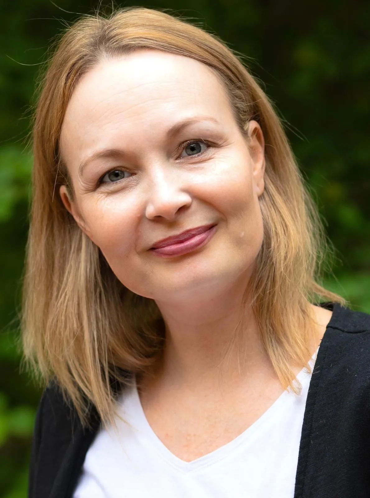 Eine Frau mit blonden Haaren und weißem Hemd lächelt in die Kamera.