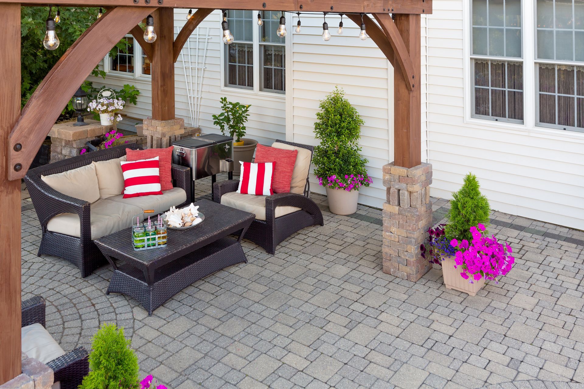 Patio with wicker furniture, pergola, string lights, and potted flowers.