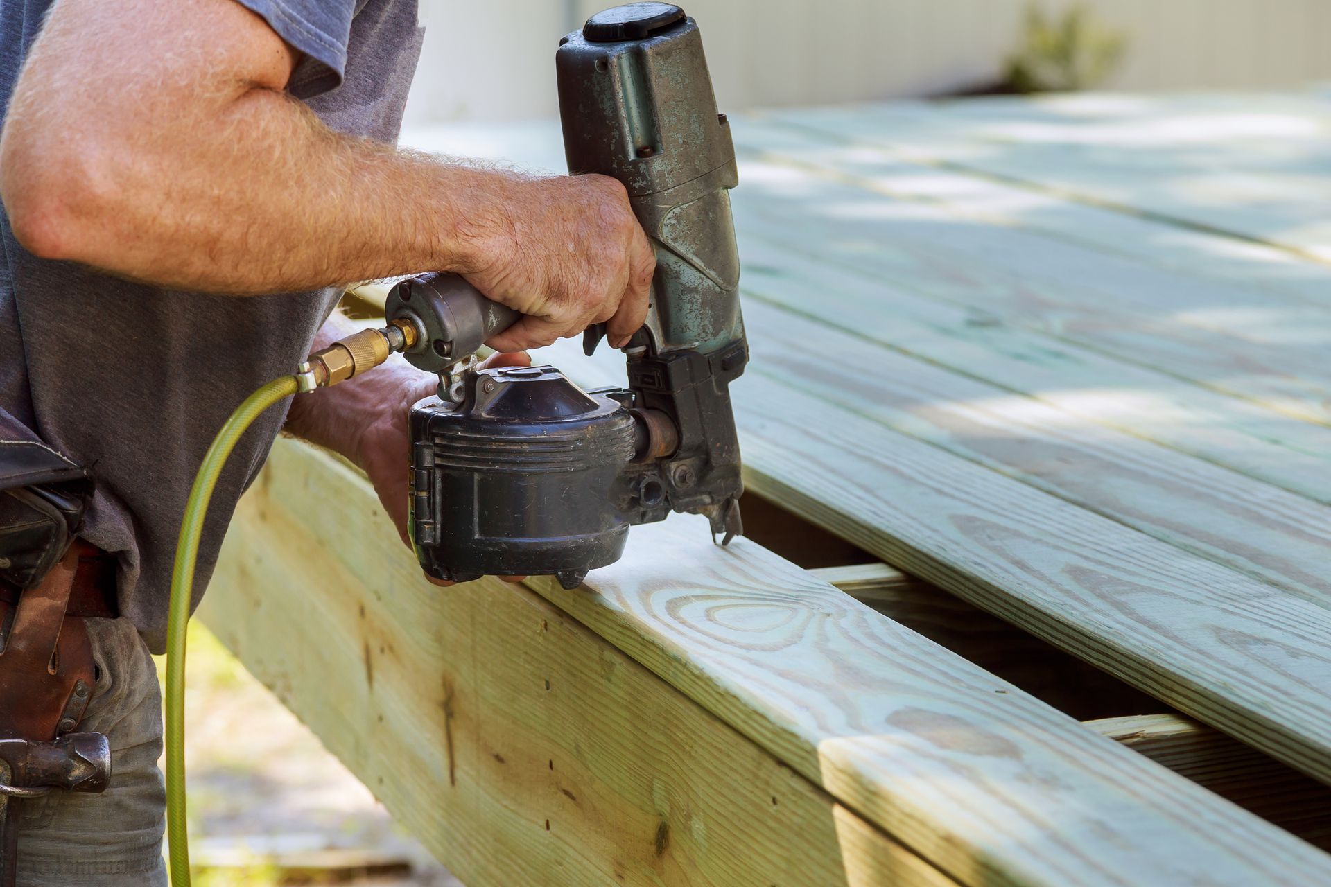 Contractor using nail gun to install wooden deck boards during professional deck construction.