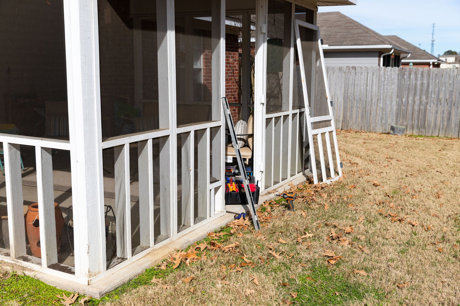 Screened porch with white frame, open door, grass lawn, and wooden fence.