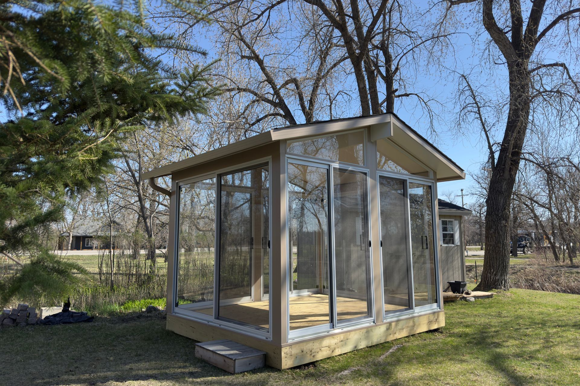 Sunroom with glass sliding doors on a grassy lawn with trees in the background.