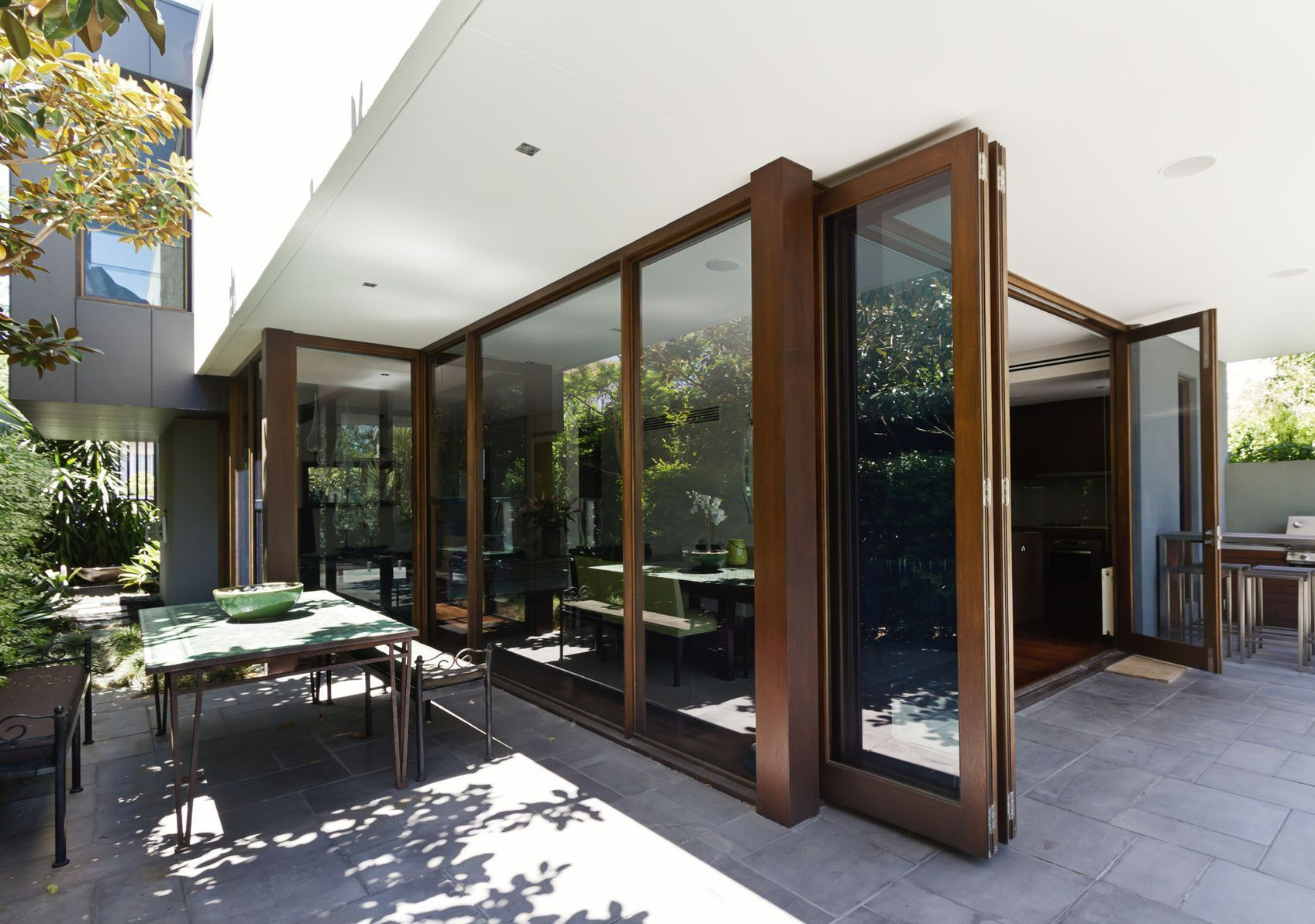 Modern patio with large glass folding doors opening to outdoor dining area and natural garden views.