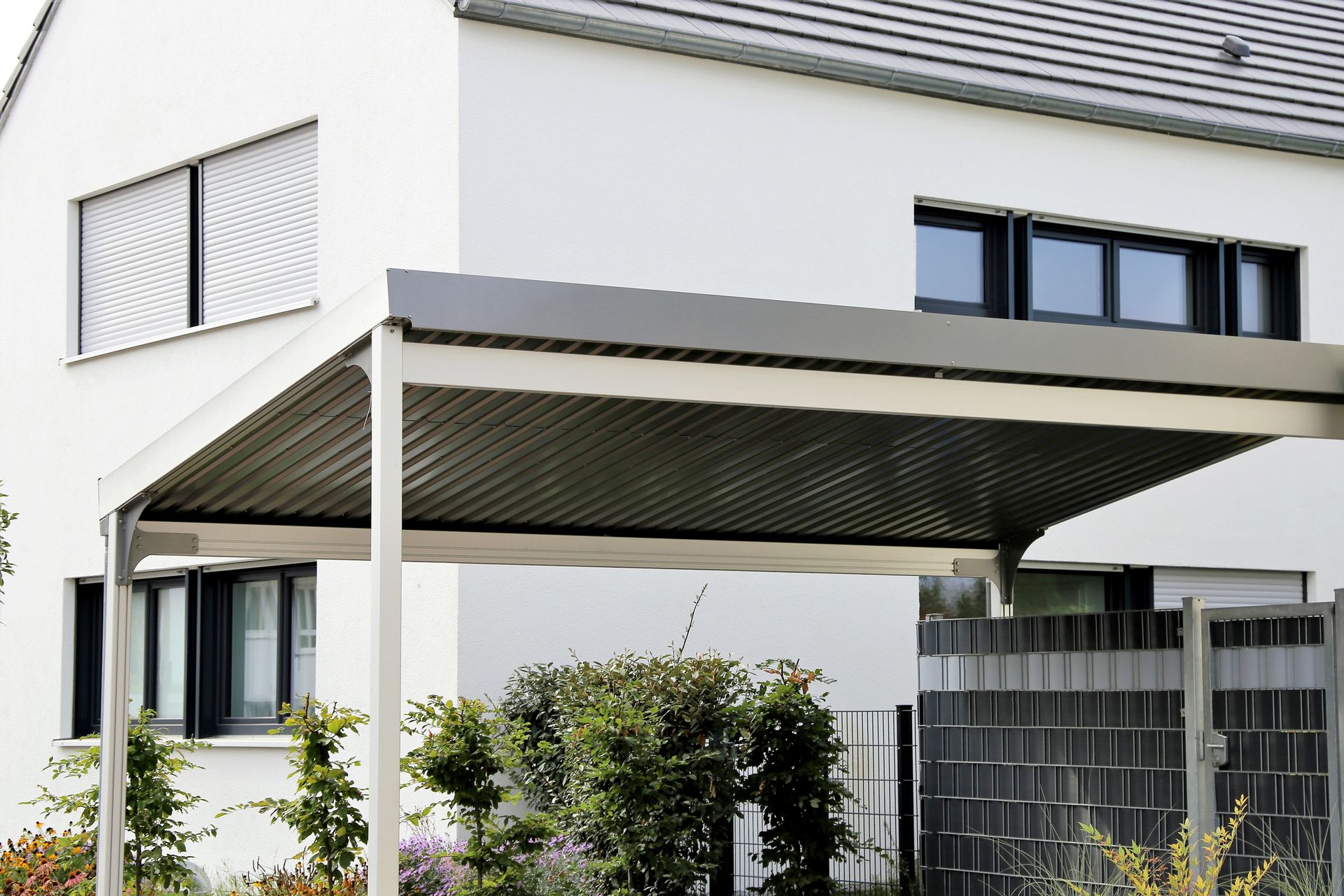 Carport attached to a white house, with a dark roof and steel frame.