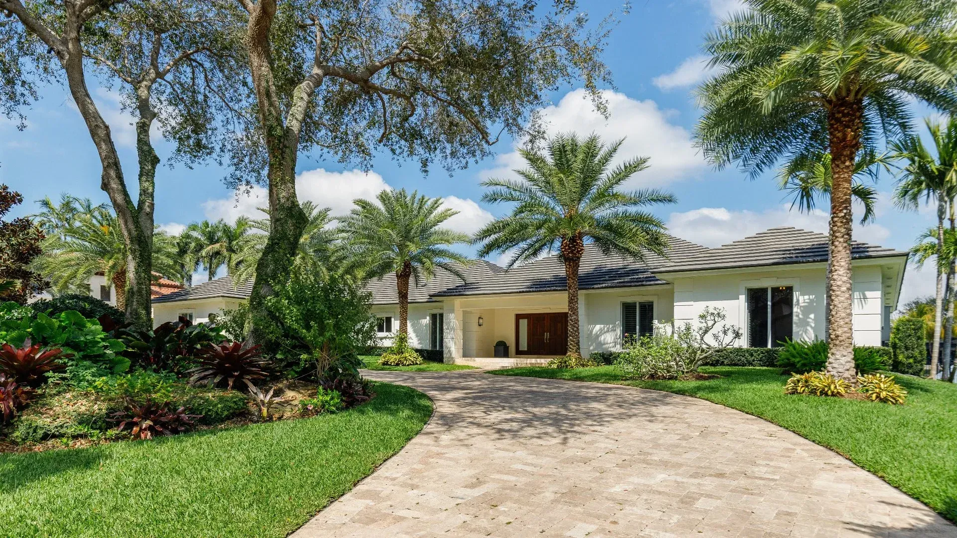 White house with palm trees, driveway, and green lawn under a blue sky.