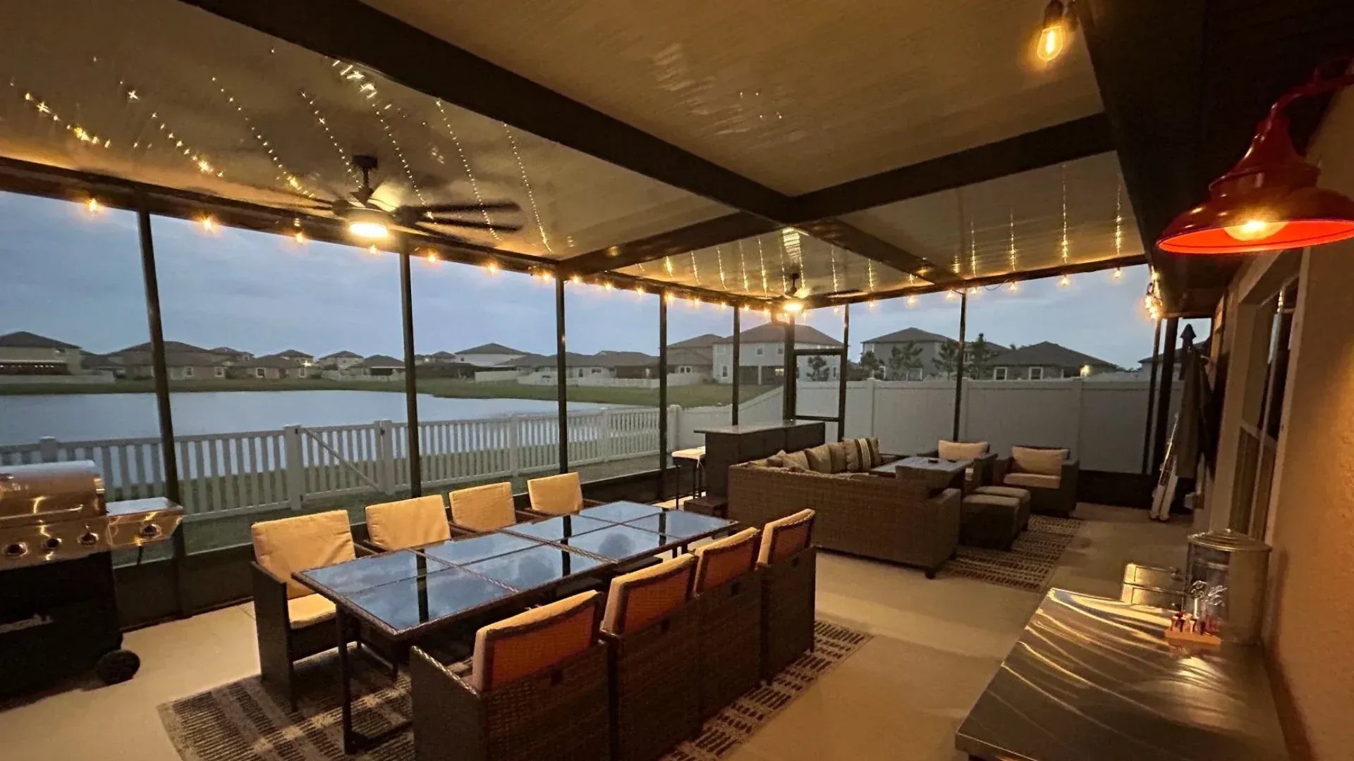Screened-in patio with string lights, dining table, seating area, and lake view during dusk. Screened-in patio overlooking lake, with dining table, seating, and string lights.