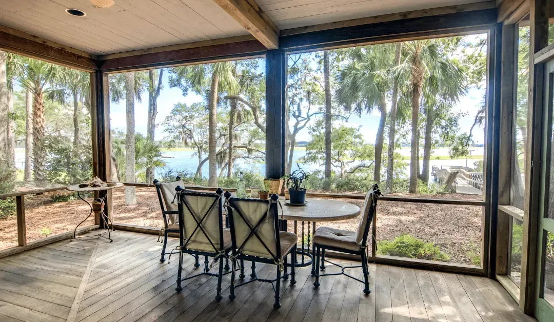 Screened porch with dining table and chairs, overlooking water and trees.