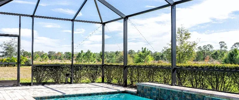Pool patio enclosed in screen with view of nature and blue sky.
