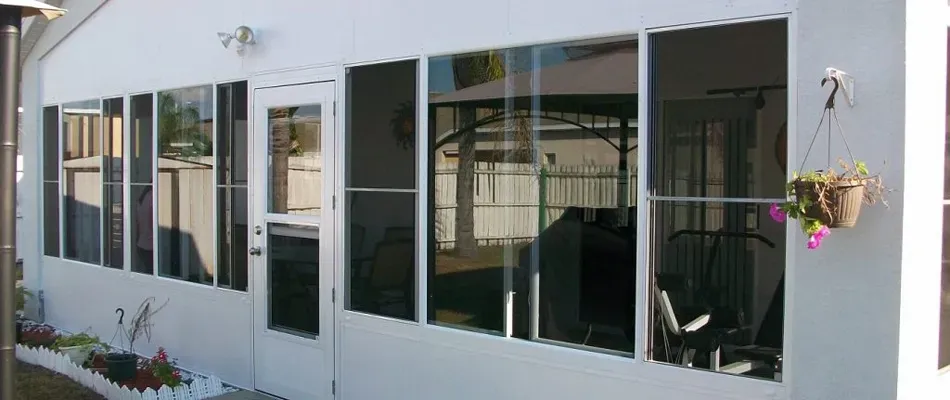 A white sunroom with screen windows, a door, and a hanging basket of flowers.
