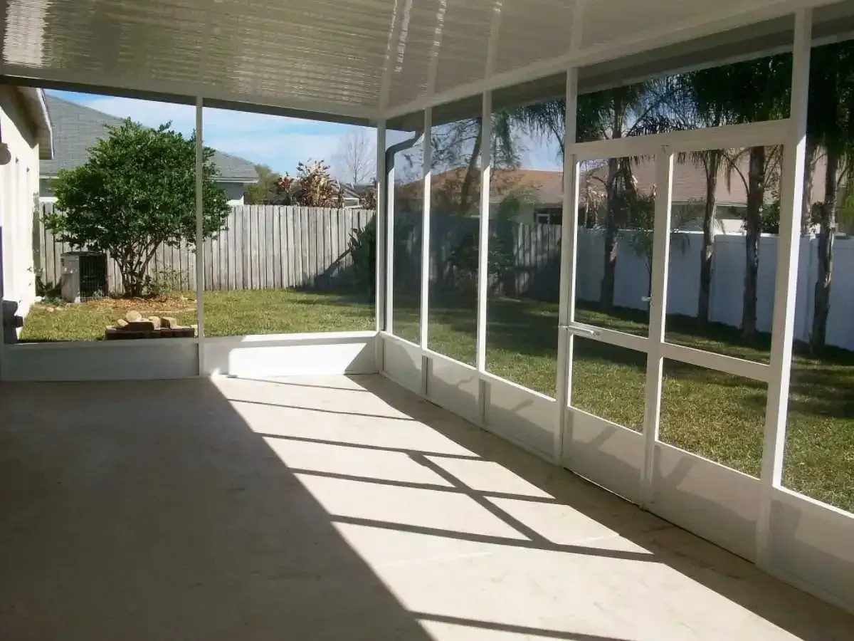 Screened-in porch with white frames, overlooking a backyard with grass, trees, and a wooden fence.
