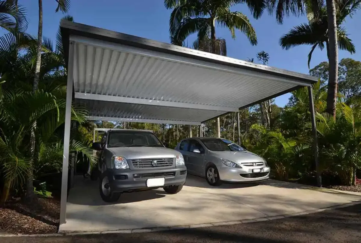Two cars parked under a metal carport in a sunny driveway.