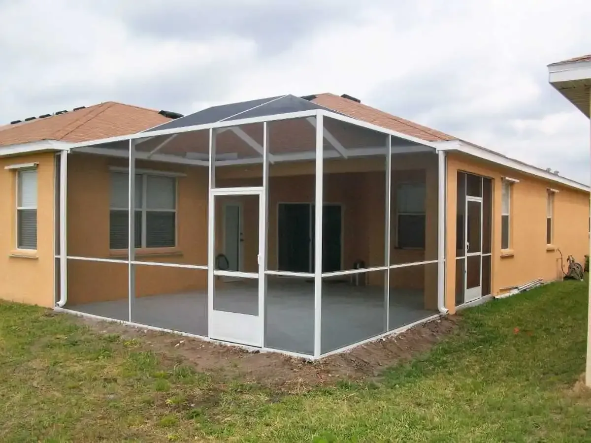 Screened-in patio extension attached to a stucco house with a light brown roof and green grass in the yard.