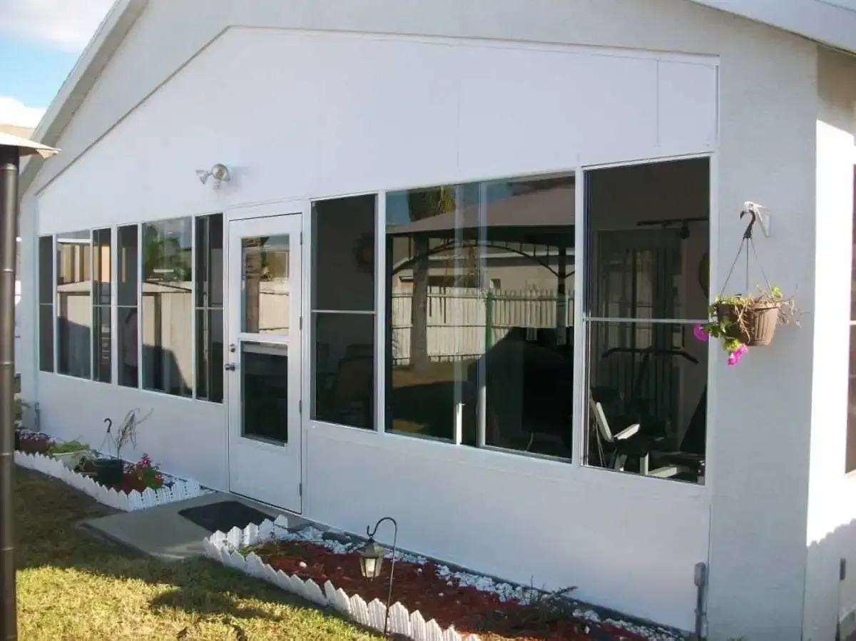 White sunroom addition with large windows, door, and potted flowers.