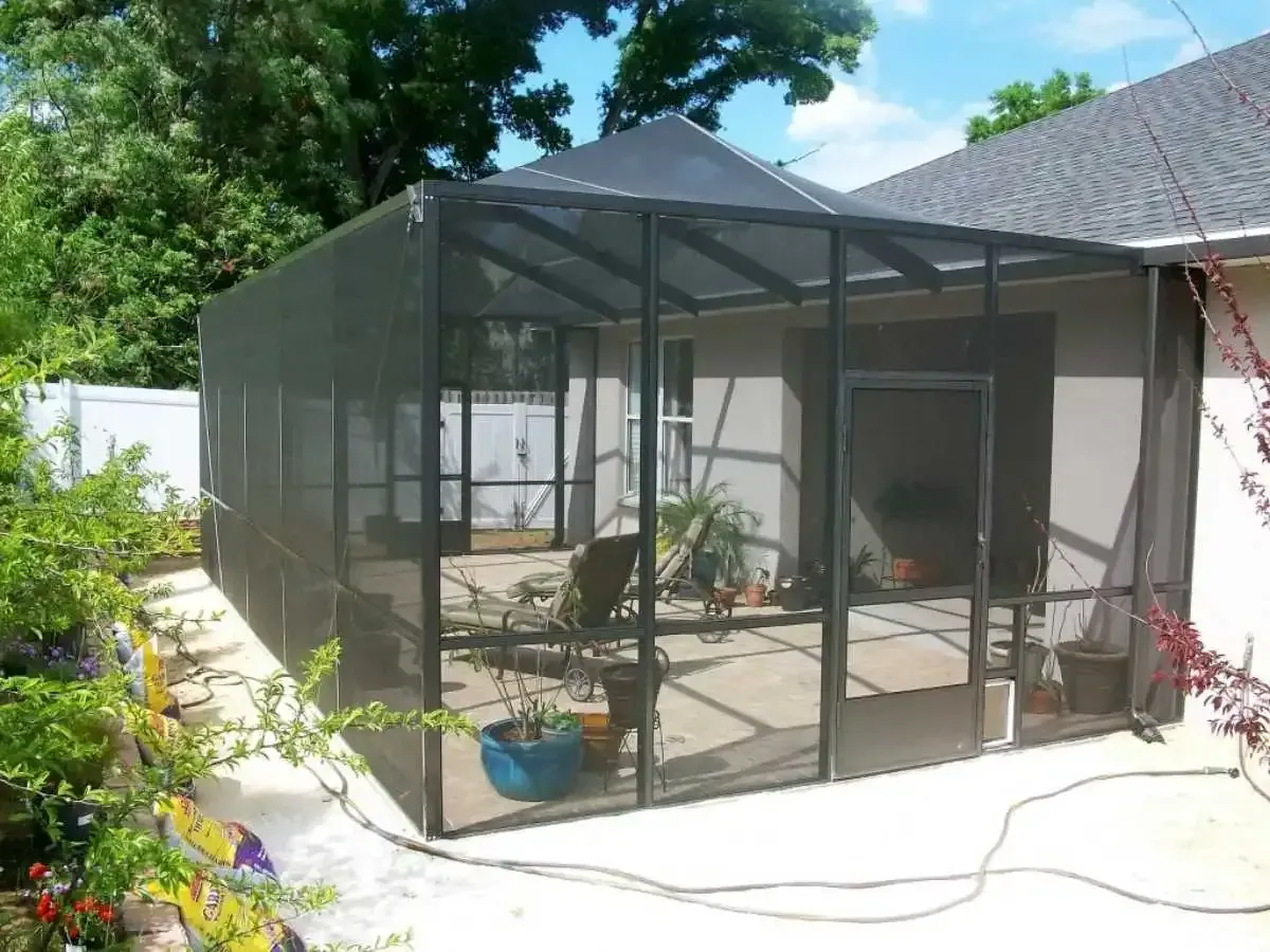 Screened-in patio with black frames and door attached to a beige house, potted plants visible.