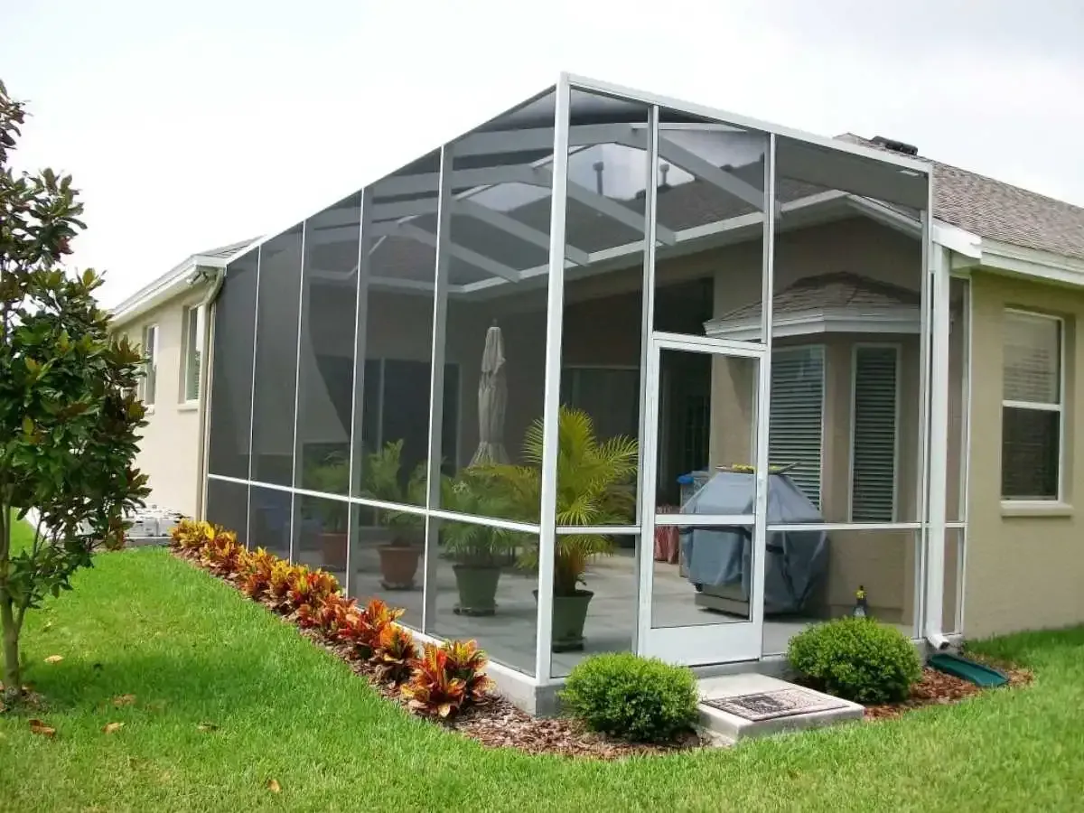 Screened-in patio extension attached to a light-colored house with potted plants and a grill.