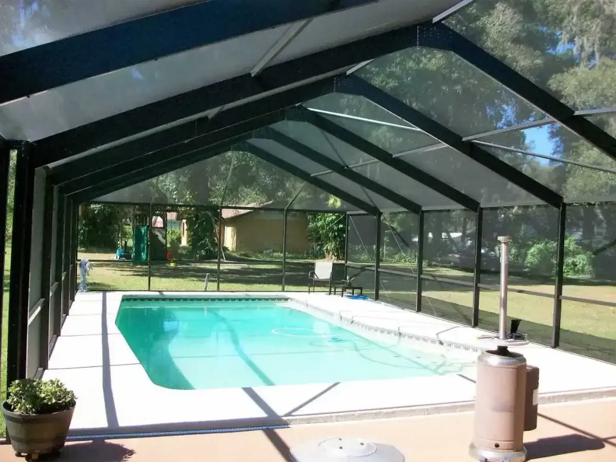 A screened-in pool with turquoise water, a black frame, and a grassy backyard.
