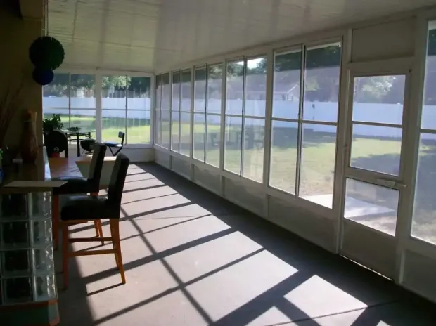 Sunroom interior with a bar and stools, looking out onto a backyard. Sunlight streams through glass windows. Sunroom interior with a bar and stools, looking out onto a backyard. Sunlight streams through glass windows.