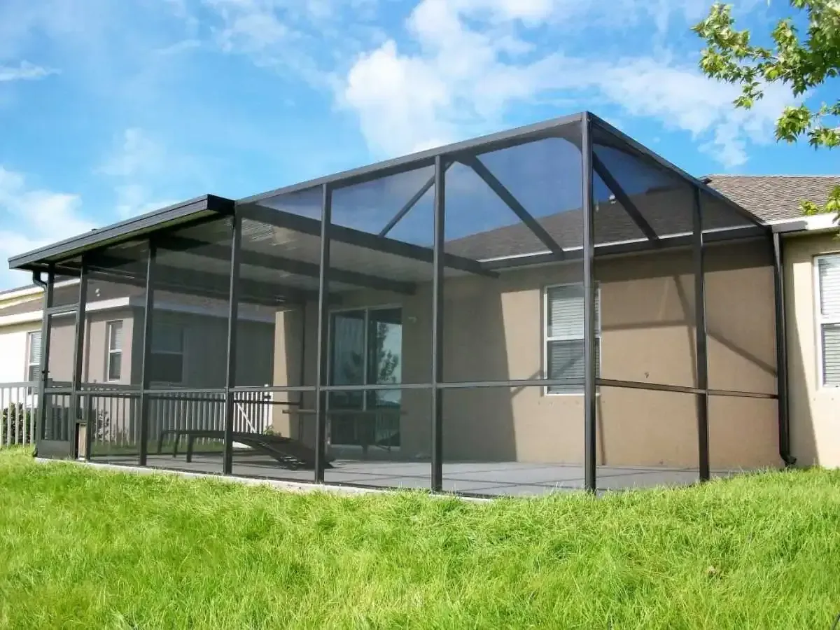 Screened-in patio extension attached to a beige house, black frame, dark screen, blue sky, and green grass.