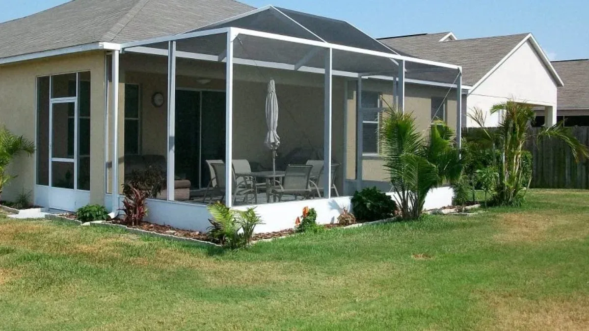 Screened patio attached to a beige house, with outdoor furniture and surrounding greenery.