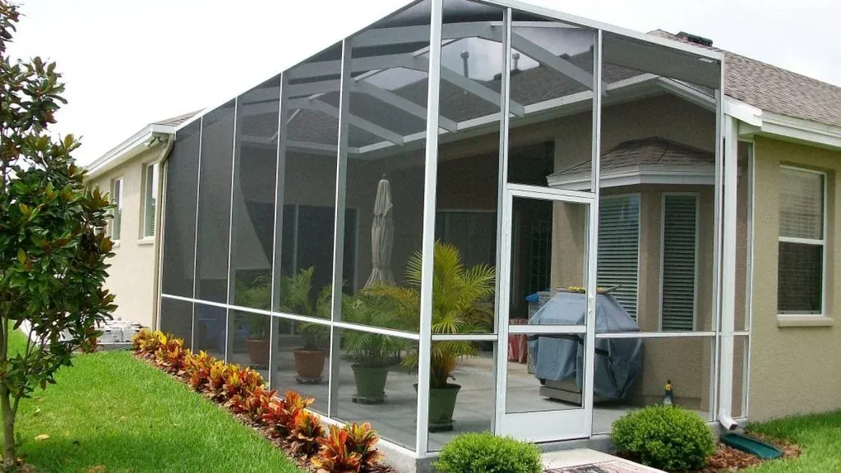 Screened-in patio extension attached to a beige house, with plants and a grill visible inside.