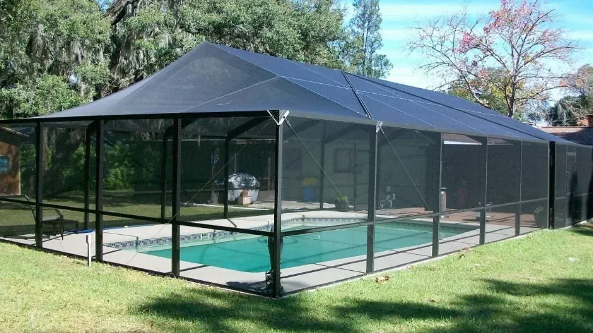 Black screened pool enclosure over a pool on a grassy lawn.