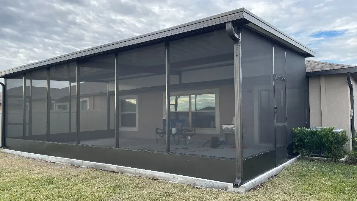 Screened-in patio extension attached to a beige house, with dark gray screens and roof.