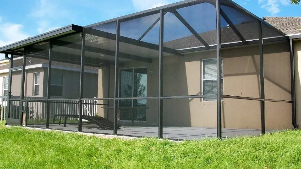 Screened-in patio with dark metal frame, on a patio next to a house, with green grass in the foreground.