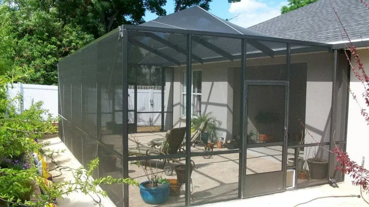 Screened-in patio extension. Black metal frame with mesh screens. Contains patio furniture, plants, and door.
