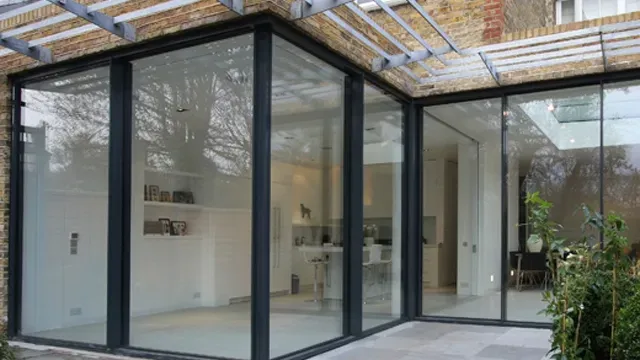 Glass-walled modern extension with black frames, attached to a brick building. Exterior patio visible.