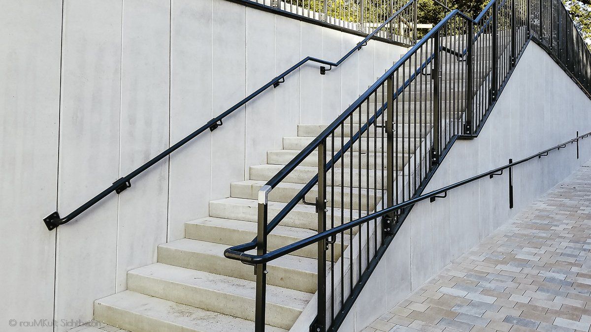 Sichtbetonkosmetik von rauMKult Sichtbeton an L-Betonwände bzw Betonsteine mit Treppe und einem schwarzen Geländer, die Betonelemente sind mit Sichtbeton Kosmetik verschönert