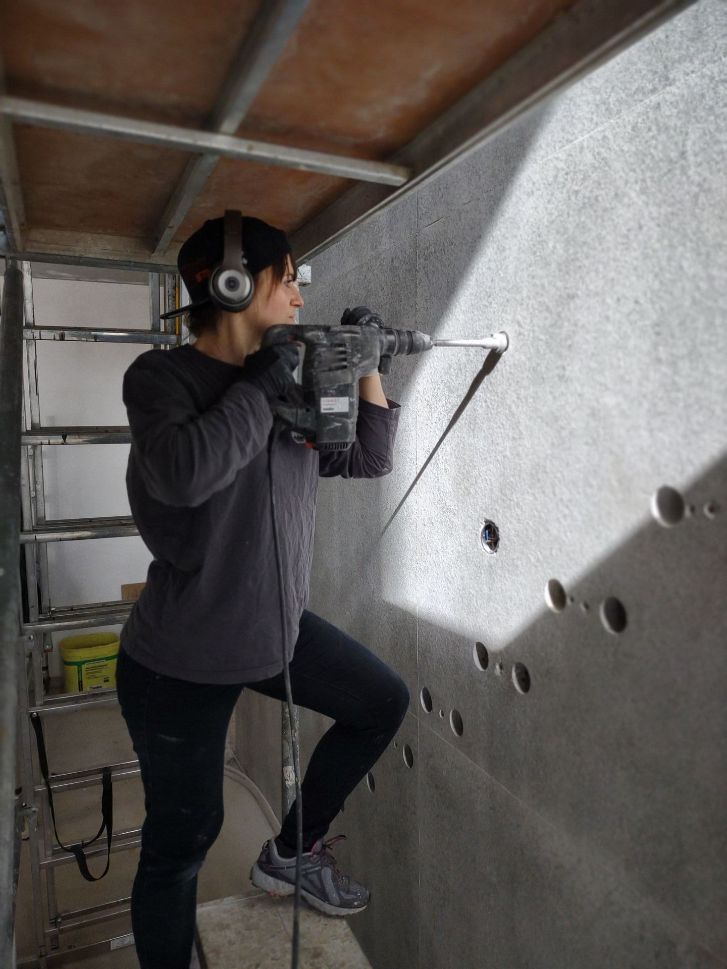 Eine Betonkosmetikerin bearbeitet Sichtbeton an einer Betonwand und bohrt Löcher für die Ankerkonen