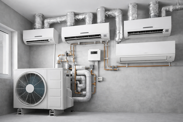 Un'unità pompa di calore bianca collegata a quattro unità interne HVAC a parete tramite tubazioni in rame e condotti isolati su una parete.