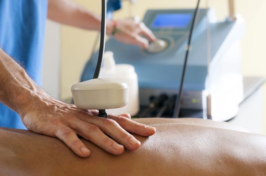 Massaggiatore che utilizza un dispositivo portatile sulla schiena di un cliente in una sala trattamenti di una spa.
