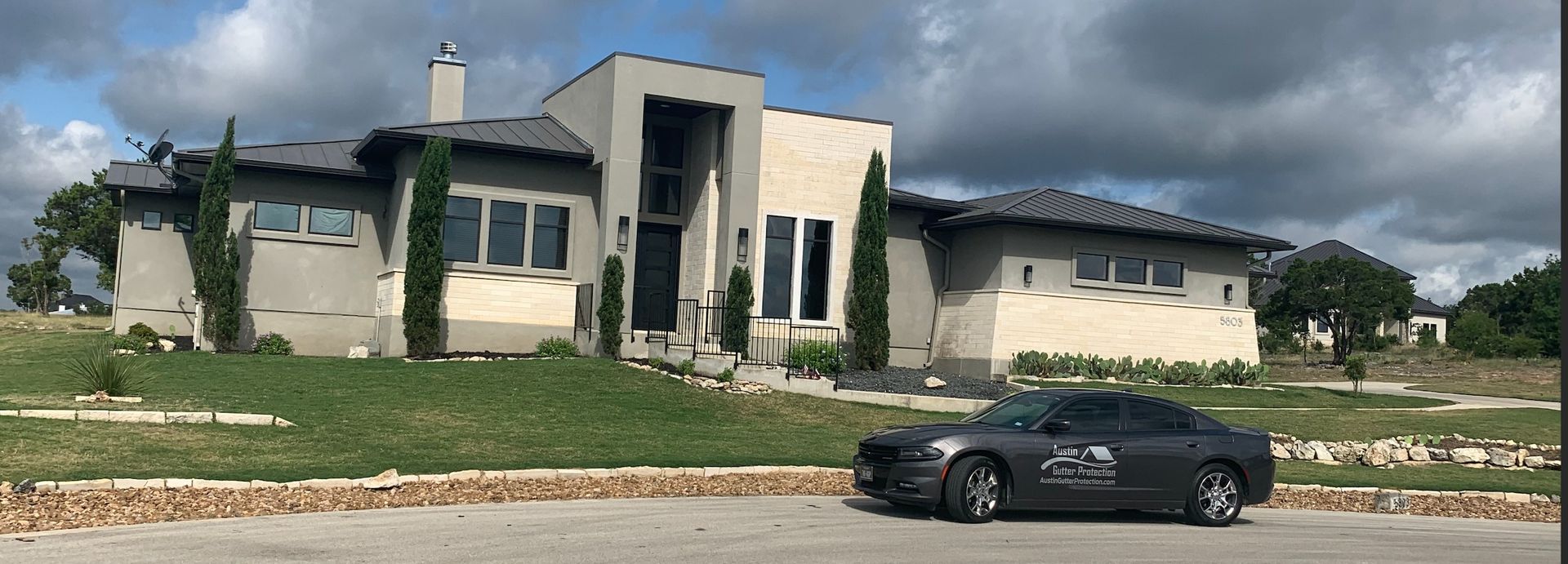 Modern house with a gray car parked in front of it under a cloudy sky.