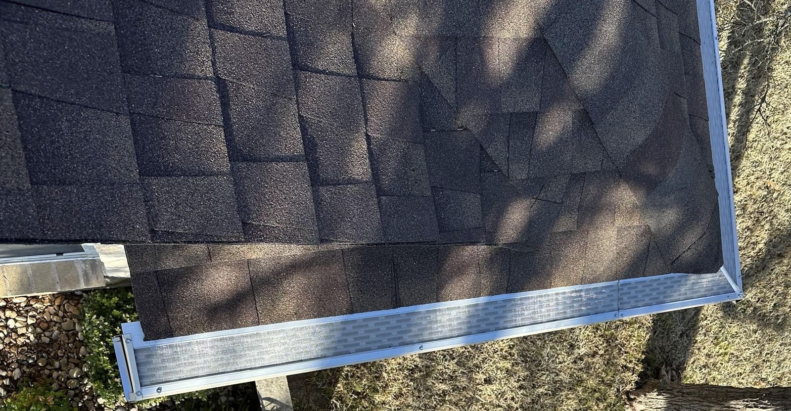 Dark shingle roof edge with silver trim and gutter, sunny outdoor setting.
