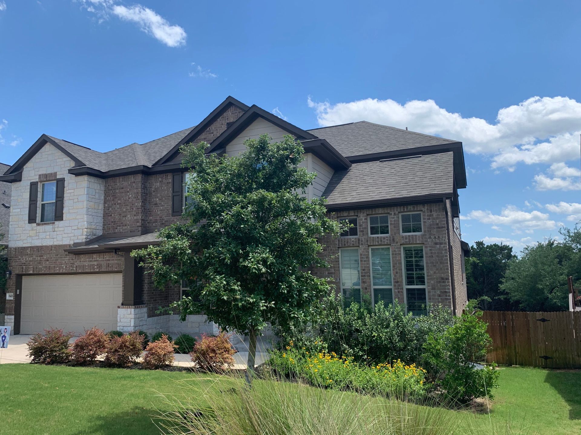 Two-story brick house with beige and brown facade, blue sky, and green yard.
