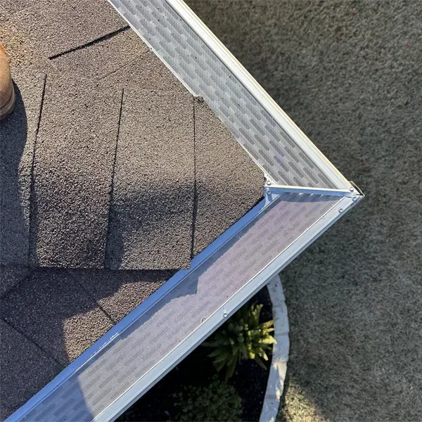 Corner of a roof with gray shingles and silver gutter.