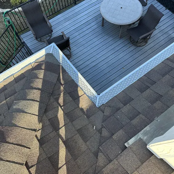 View of a brown shingled roof next to a gray deck with a table and chairs.