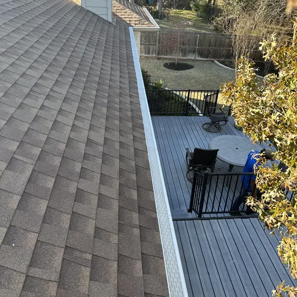 Overhead view of a house roof next to a gray deck with black railing. Backyard in background.