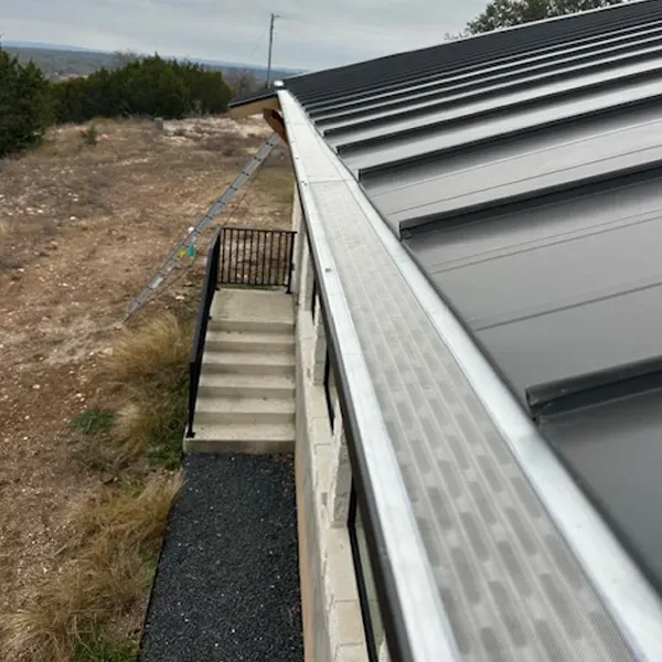Black metal roof with gutter guard; stone house with steps and gravel, outdoor setting.