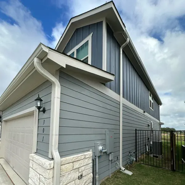 Side view of a two-story house with blue-gray siding, beige trim, and a detached garage with a white door.
