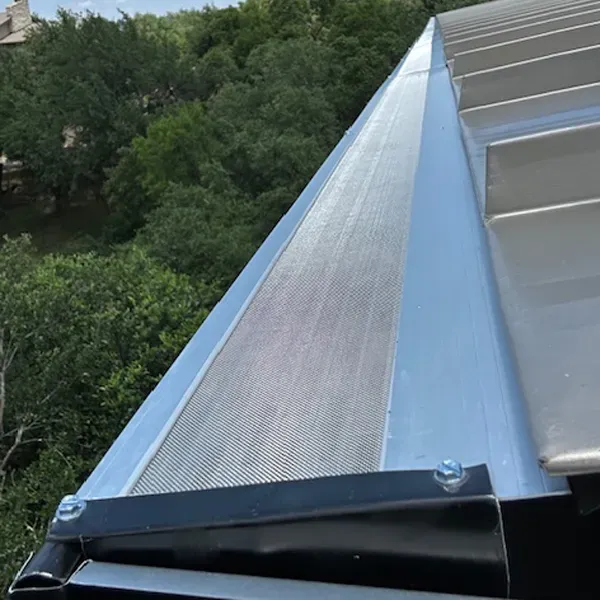 Close-up of a metal roof with gutter guard; silver metal against green foliage.