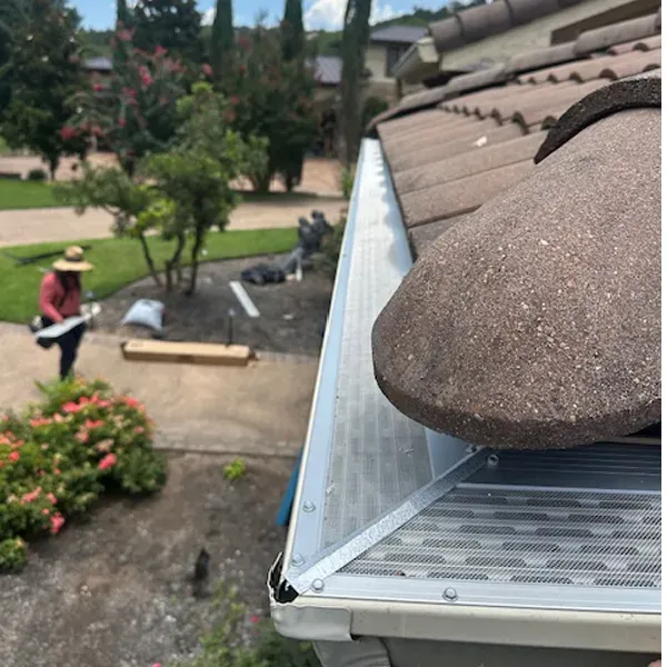 Gutter guard installation on a residential roof, with a worker in the background.