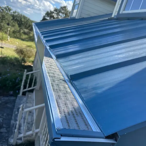 Blue metal roof with gutter guard installed on a house, angled view.
