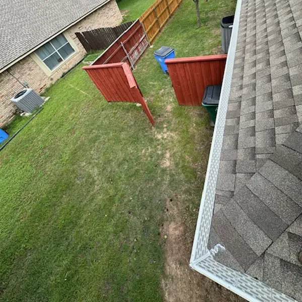 View from roof of green backyard with fence, trash cans, and house.