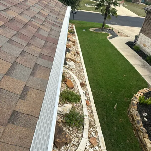 A sloped brown roof with gutter next to a rock garden and green lawn, viewed from above.