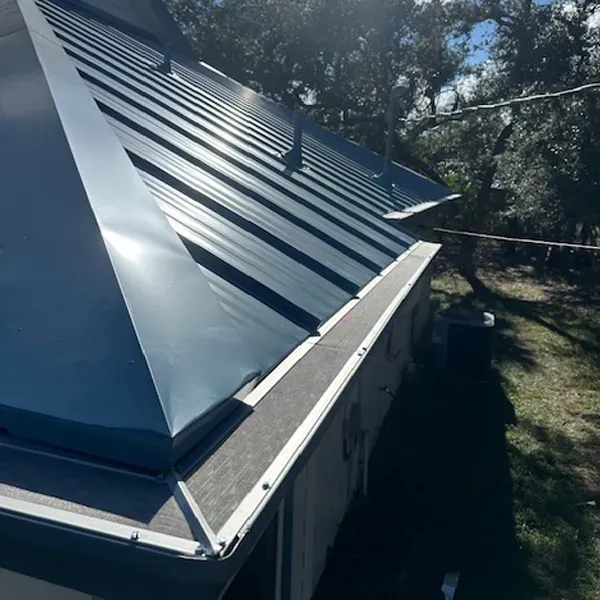 Dark blue metal roof on a building, angled view, with trees in the background.